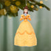 Ornament of a character in a yellow dress against a blurred green background