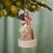Ornament of a character holding a paddle, hanging from a tree with a blurred green background.