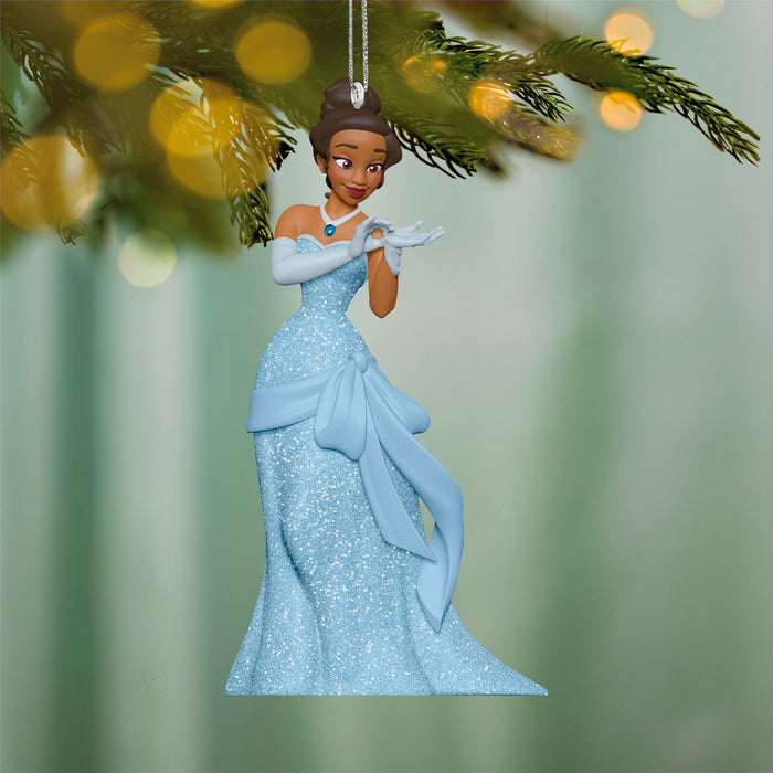 Ornament of a princess in a blue gown hanging on a tree branch with blurred lights in the background