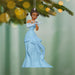 Ornament of a princess in a blue gown hanging on a tree branch with blurred lights in the background