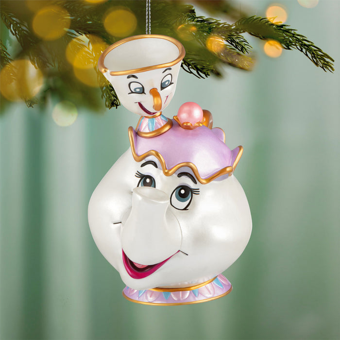 Decorative ornament shaped like a teacup with a smiling face, hanging on a Christmas tree.