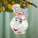 Decorative ornament shaped like a teacup with a smiling face, hanging on a Christmas tree.