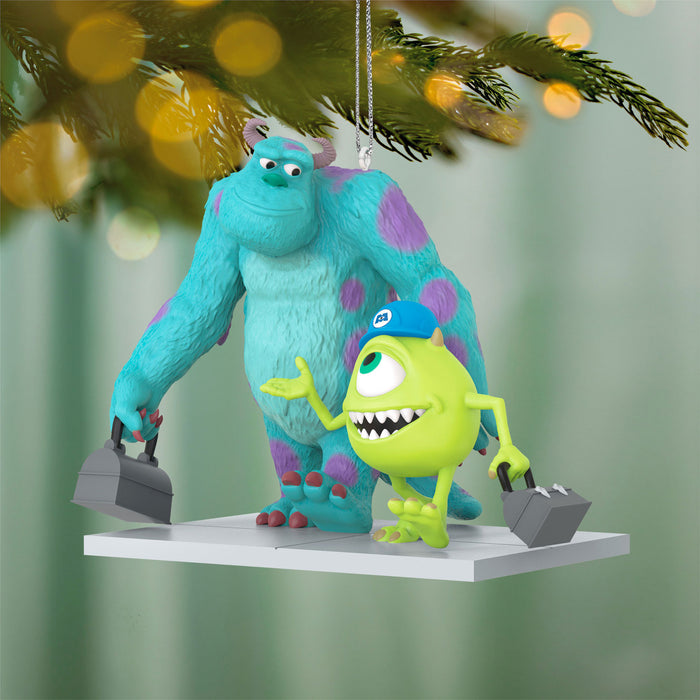 Decorative ornament featuring two animated monster characters on a Christmas tree with blurred lights in the background.