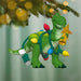 Green dinosaur Christmas ornament with lights and a star, hanging on a tree.