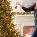 Person decorating a Christmas tree with  an ornament in a festive living room.