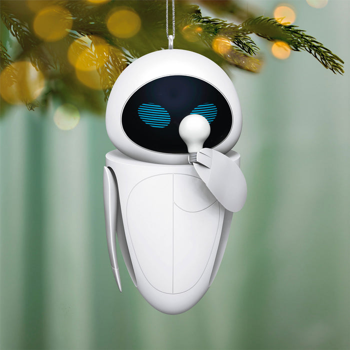 White robot ornament with blue eyes hanging on a Christmas tree.