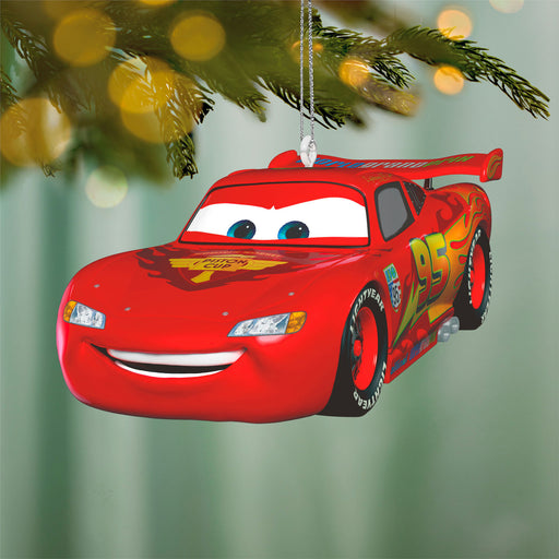Red car-shaped Christmas ornament hanging on a tree branch with blurred lights in the background