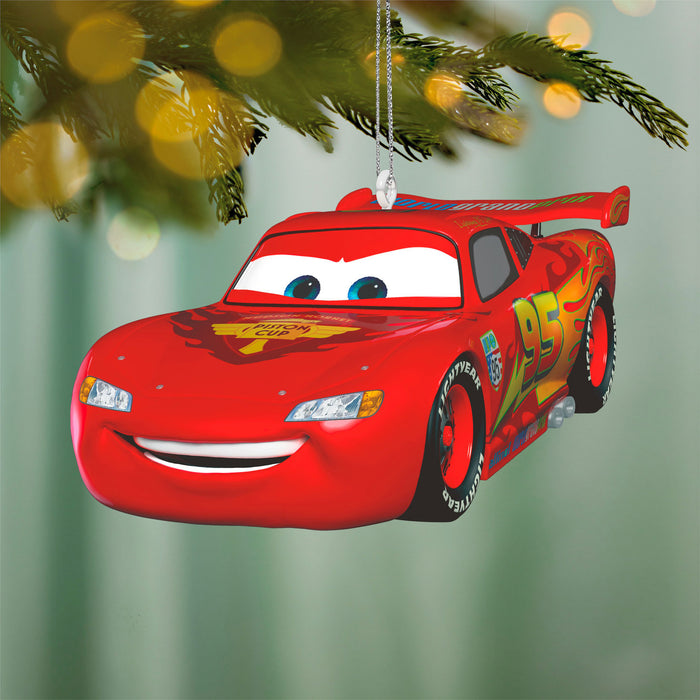 Red car-shaped Christmas ornament hanging on a tree branch with blurred lights in the background