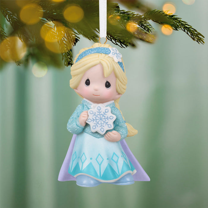 Decorative Christmas ornament of a girl in a blue dress holding a snowflake, hanging from a tree.