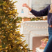 Person decorating a Christmas tree with a small ornament in a festive living room.