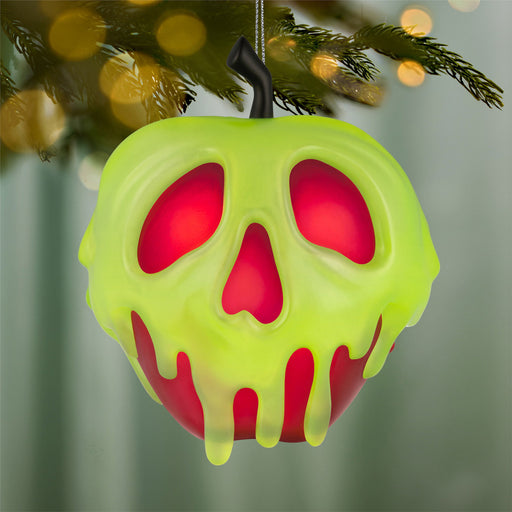 Decorative ornament shaped like a green apple with red interior, resembling a skull, hanging on a Christmas tree.