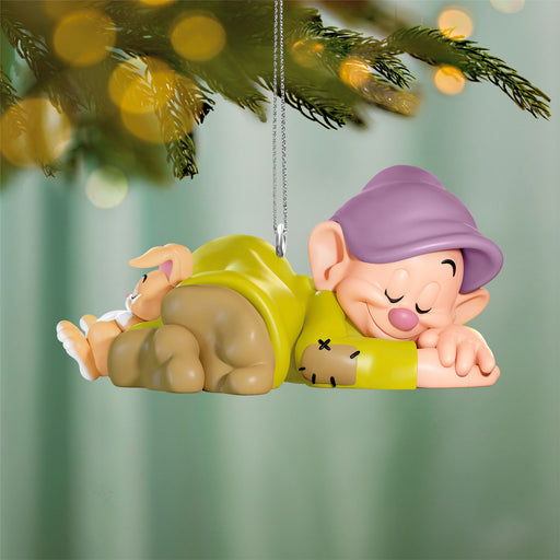 Animated character ornament hanging from a Christmas tree with blurred lights in the background