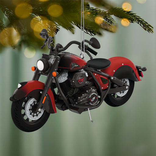 Red and black motorcycle ornament hanging on a Christmas tree with blurred lights in the background.