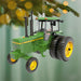 Green tractor ornament with yellow wheels hanging on a Christmas tree.