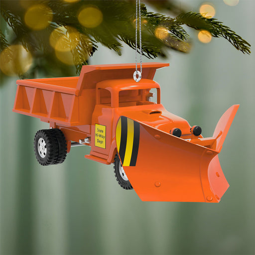 Orange snow plow ornament hanging on a Christmas tree with blurred lights in the background