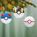 Three Poké Ball ornaments hanging on a Christmas tree with a blurred green background.