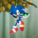 Sonic the Hedgehog Christmas ornament holding a green gem, hanging on a tree with blurred lights in the background.