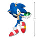 Blue animated character with red shoes holding a green gem on a white background
