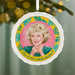 Decorative ornament with a portrait of a woman and text, hanging on a Christmas tree.