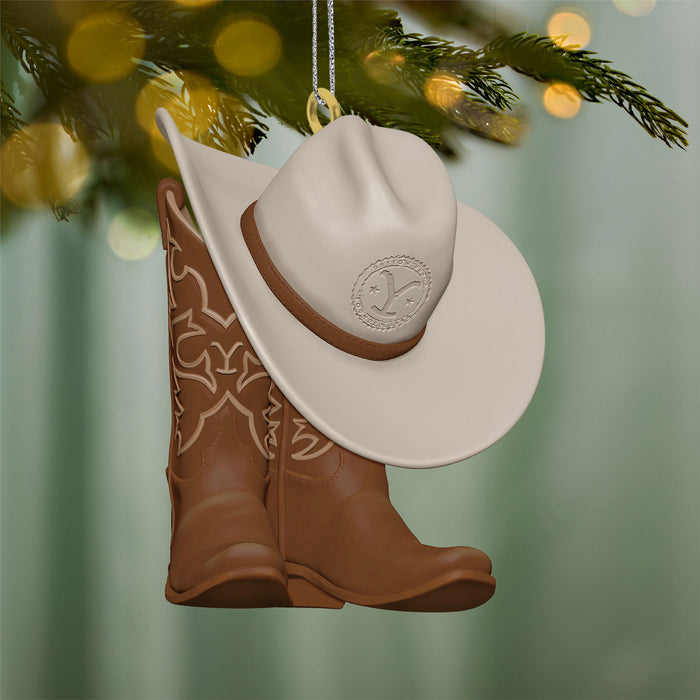 Decorative ornament with cowboy hat and boots hanging on a tree branch.