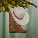 Decorative ornament with cowboy hat and boots hanging on a tree branch.