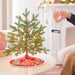Small decorated Christmas tree with a hand placing a toy train on it in a cozy living room.
