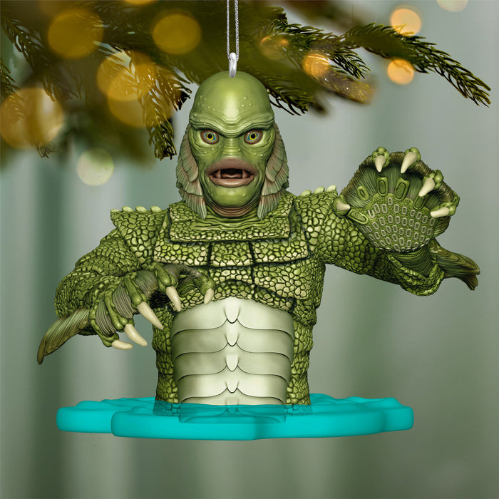 Green creature ornament hanging on a Christmas tree with blurred lights in the background