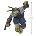 Toy figure of a character with a blue outfit and green face, holding weapons, on a white background with dimensions indicated.