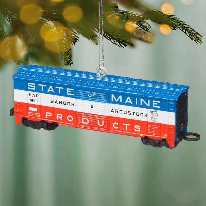 Decorative train car ornament with 'State of Maine' text, hanging on a Christmas tree.