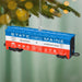Decorative train car ornament with 'State of Maine' text, hanging on a Christmas tree.