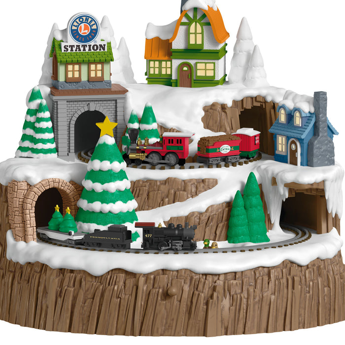 Toy train set with a snowy village scene featuring buildings and trees.