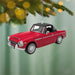 Red convertible car ornament hanging on a Christmas tree branch with blurred lights in the background.