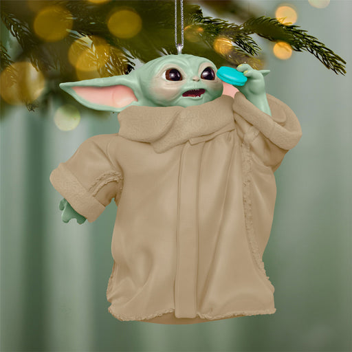Decorative ornament of a character in a beige coat hanging on a tree branch with blurred lights in the background.