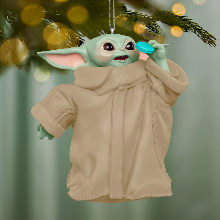 Decorative ornament of a character in a beige coat hanging on a tree branch with blurred lights in the background.