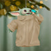 Decorative ornament of a character in a beige coat hanging on a tree branch with blurred lights in the background.