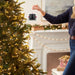 Person adjusting a smart home device near a decorated Christmas tree.