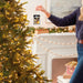 Person hanging a decorative ornament on a Christmas tree in a festive living room.