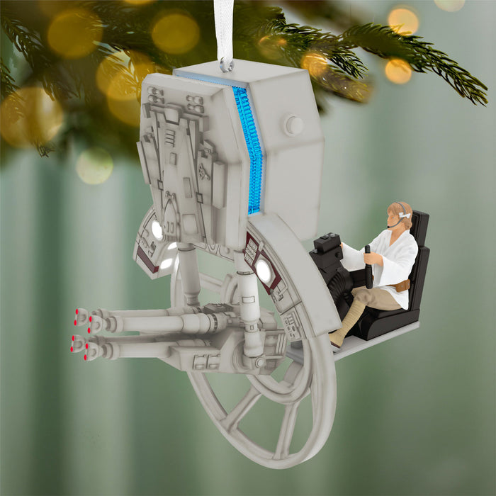 Decorative ornament resembling a spaceship with a figure inside, hanging on a Christmas tree.