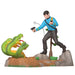 Figurine of a character in a blue shirt and black pants standing on a rock with a green snake and a gun.