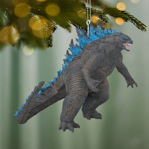 Godzilla ornament with blue spikes hanging on a Christmas tree.