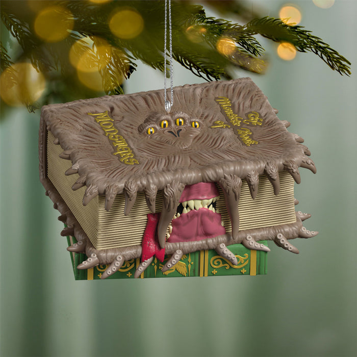 Decorative ornament shaped like a book with a monster design, hanging on a Christmas tree.