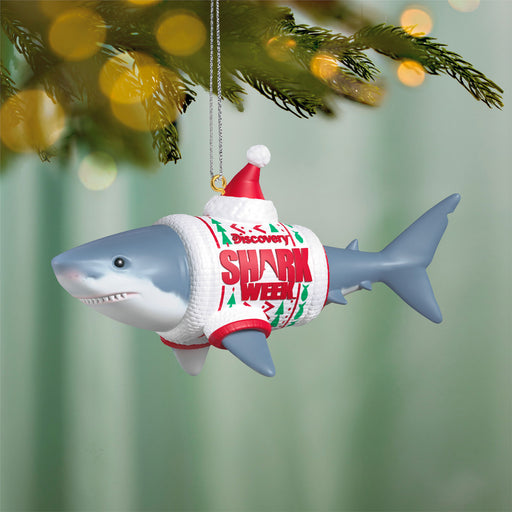 Shark ornament wearing a sweater with 'Shark Week' text, hanging on a Christmas tree.