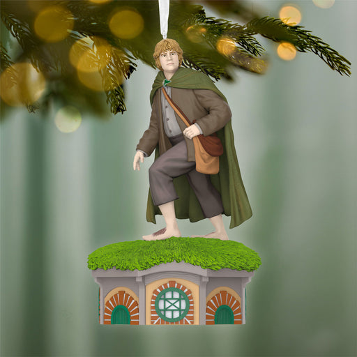 Ornament of a character in a green cloak standing on a small building with a green roof, against a blurred forest background.
