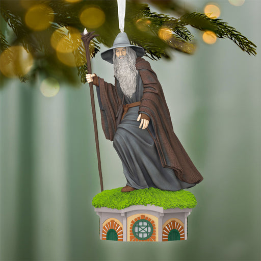 Ornament of a character in fantasy attire with a staff, standing on a small platform with a green roof and brick design, against a blurred natural background.