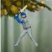 Baseball player ornament in a gray uniform with a blue helmet, holding a bat, hanging from a Christmas tree.