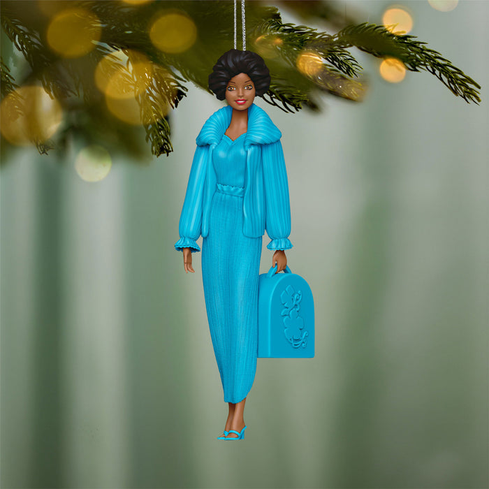 Decorative ornament of a woman in a blue outfit holding a suitcase, hanging from a tree.