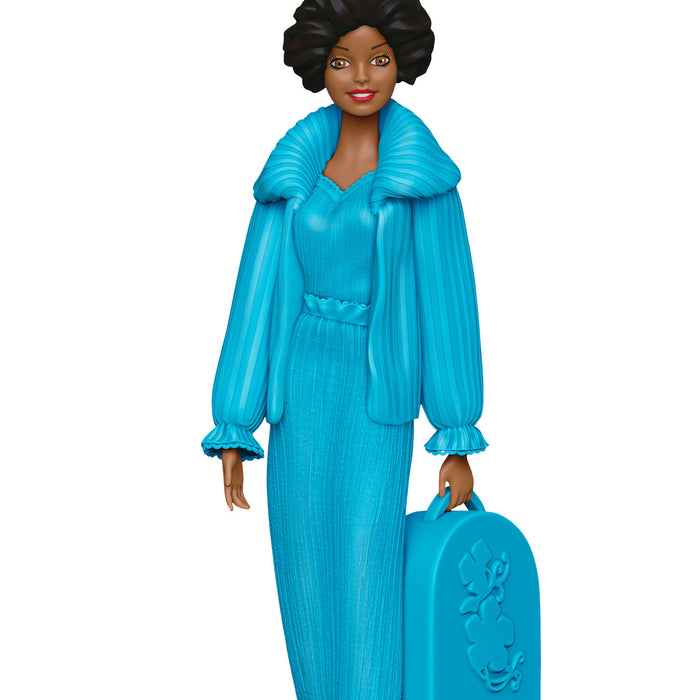 Toy figure of a woman in a blue outfit holding a matching suitcase on a white background