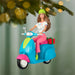 Decorative ornament of a woman on a scooter with a gift, hanging from a tree.
