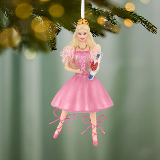 Decorative ornament of a Barbie in a pink dress holding a nutcracker, hanging on a Christmas tree.