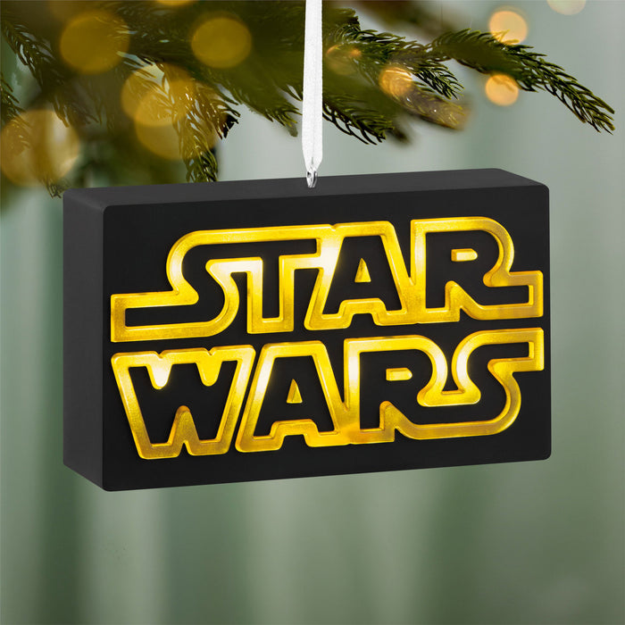 Star Wars logo ornament hanging on a Christmas tree with blurred lights in the background